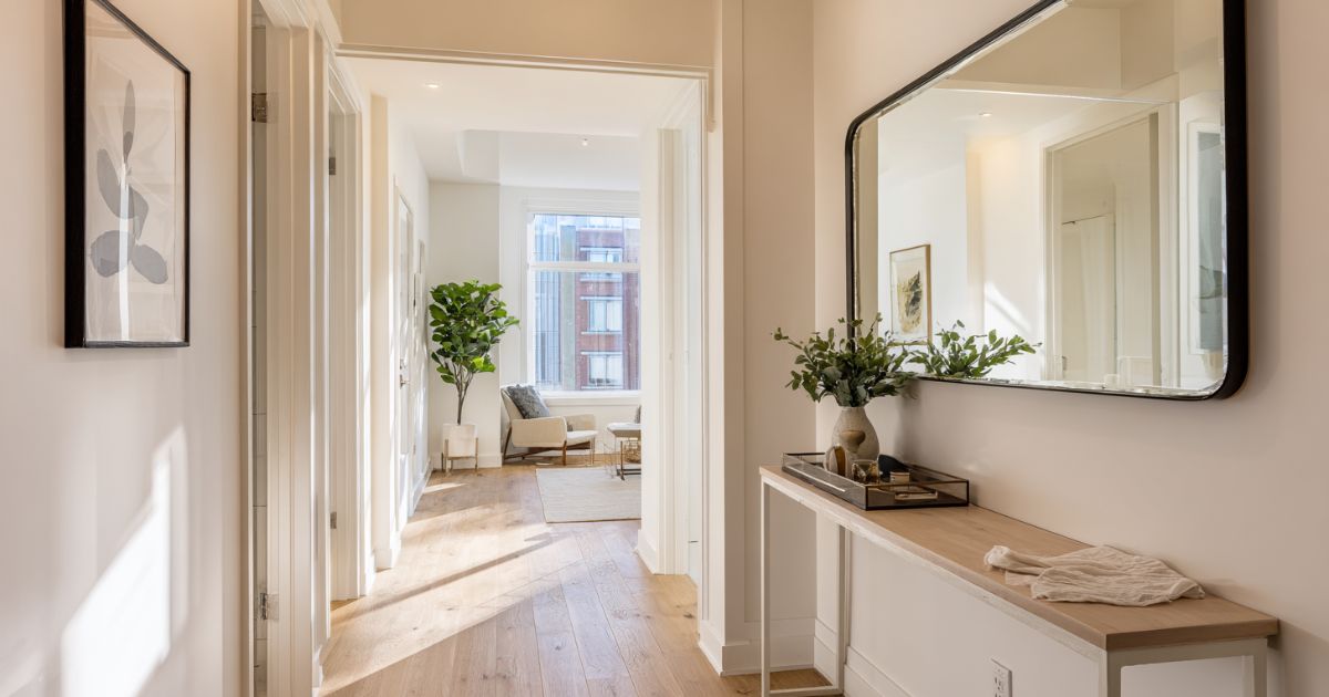 Bright apartment entryway with large mirror reflecting natural light from opposite window making the narrow space feel open and spacious